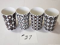 Four tall Maxwell Williams coffee mugs in Marakesh design with varied brown and black geometric patterns shown side by side.