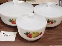 Set of 3 vintage Federal Glass milk glass mixing bowls with lids, each featuring fruit decals, photographed on wooden surface.
