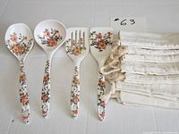 Set of 4 floral kitchen utensils and 6 cream-colored cloth drawstring bags on white surface.