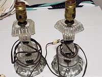 Photo showing front view of the two vintage clear glass table lamps, both without shades, with original brown cords coiled around the bases.