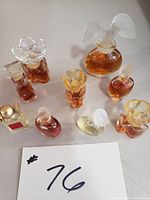 Photo showing nine assorted small perfume bottles with different shapes, containing varying amounts of amber and clear liquid.