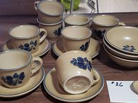 Photo showing Pfaltzgraff cups stacked with saucers and bowls with a beige base and blue floral pattern.