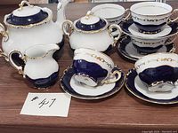 Full view of tea set including teapot, creamer, covered sugar bowl, several cups and saucers displaying blue and gold Pompadour pattern