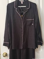 Front view of the black satin jacquard pajama top showing pink piping detail and embroidered logo on chest pocket