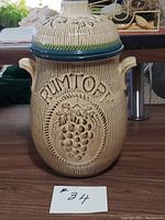 Front view of ceramic Rumtopf jar with lid showing embossed grape design and lettering.