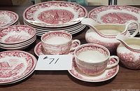 Full set of plates and serving pieces arranged on table showing pink transferware with Currier & Ives American Subject designs and floral borders.