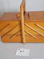 Side view of vintage wooden accordion style sewing box with handle showing expanding compartments closed.