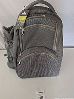 Front side of the black picnic backpack with tags still attached, showing multiple zippered pockets and padded handle