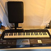 Full view of Casio electronic keyboard, adjustable stand underneath, and padded black bench.
