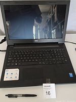 Full view of Dell laptop with keyboard, screen, and wrist rest area showing the Intel Core i5 and other specification stickers, alongside a pen for scale.