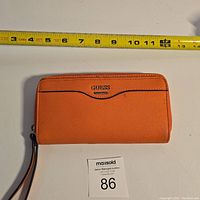 Front view of orange Guess wallet with measuring tape showing approximately 7.5 inches width.