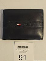Closed view of the black leather wallet with embossed logo and flag detail on front.