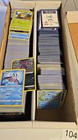 Long cardboard boxes filled with stacks of Pokemon cards, mostly Japanese with some energy cards, neatly arranged.