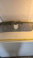 Full view of the Night Cat tent carrying bag with logo and handle strap, laid flat with a measuring tape showing approximately 22 inches in length.