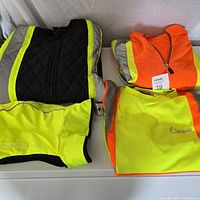 Overview of four folded high visibility garments: black quilted winter jacket with neon yellow and reflective gray stripes, neon orange fleece top with zipper, neon yellow-green fleece with orange trim and Ottawa branding, and neon yellow-green hood accessory.