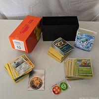 Overview of lot showing multiple piles of Pokemon cards, card box, small card binder, bird-themed token, and green/orange circular tokens