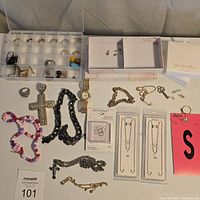 Wide shot of the jewelry lot including rings, large cross pendant necklace, thick chain necklace, beaded necklaces, stud earrings, and pendants.