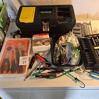 Overview of toolbox with various tools including pliers, screwdrivers, bungee cords, hardware parts, clamps, and tape on a table