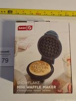 Front view of the original boxed Dash Snowflake Mini Waffle Maker showing packaging with image of product and key features.