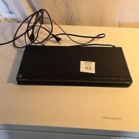 Sony Blu-Ray and DVD player viewed from front showing unit and attached power cord on white Frigidaire surface.