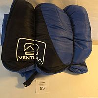 Blue Ventura sleeping bag rolled in black Ventura carrying bag with logo visible in first photo