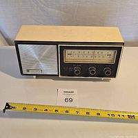 Front and top view showing the body with cream top and black sides, silver speaker grill, AM/FM frequency dial, and three control knobs.