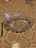 Clear crystal bowl platter with decorative starburst and geometric cut patterns, displayed on patterned tile floor.