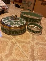 Three green crystal bowls arranged on floor, one with lid and crystal knob, each featuring white classical figures and gold trim