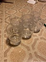 Photo showing all six crystal glasses arranged on a patterned surface, clear glass with geometric cuts visible.