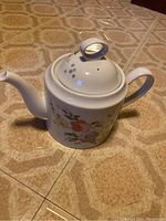 Full view of white porcelain tea pot with floral decoration and fitted lid