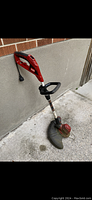 Photo of red and black Toro electric grass trimmer leaning against a brick wall, showing the handle with power cord and trigger.