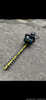 Full view of electric hedge trimmer laid on pavement showing full yellow-and-black dual-sided blade, handle and cord.