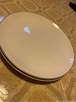 Stack of two creamy white Iron Stone Kokura Ware plates with subtle rim detail on patterned surface.