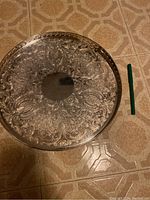 Top-down photo of large round Sheffield plate tray showing detailed floral engraving and pierced rim with pen for scale.