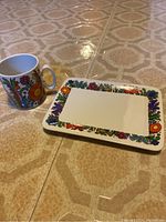 Photo showing the plate and mug with vivid, colorful designs on a tiled floor.
