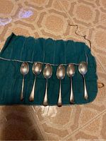 Six silver spoons laid out side-by-side on green fabric holder, showing the shape and length of spoons.
