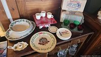 Full view of the Christmas dish set items arranged on a wooden surface, showing plates, cups, platters, bowl, candle holder, and boxed Serve-A-Snack sets