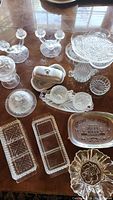 Top view of assorted clear crystal serving dishes, rectangular trays, a floral bowl, candle holders, and a white Lenox butter dish with lid.