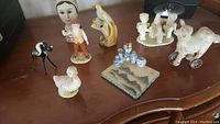Top view showing all 8 figurines including man with skull, bird on coral, deer, duck, camel on wheels, and blue and white ceramic items.