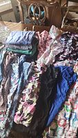 Multiple nurse scrub tops and pants in various solid colors and floral patterns laid out on table.