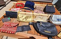 Multiple purses and clutches displayed on a wooden surface in bright daylight showing variety of colors, materials, and styles.