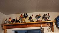 Full view of 10 rooster and hen figurines displayed on a wooden shelf, showing variety in size, color, and pose.