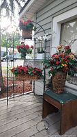 Silk plant arrangements including red flower baskets on metal plant stand and large flower arrangement in woven vase.
