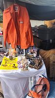 Full view of table showing multiple sports memorabilia, orange Denver Broncos jacket on left, baseball gloves, collectible items and a collage artwork featuring Babe Ruth.
