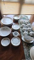 Overview of entire fine china set arranged on a dining table showing plates, bowls, cups, saucers, and gravy boat.