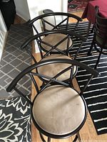 Three cafe bar stools arranged in a row showing black metal curved backrests and beige round seats with some staining
