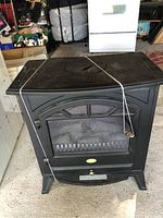 Front view of black electric fireplace heater with windowed door and metal handle, secured by string and visible scratches on surface.