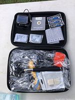 Overview photo showing GoPro HERO+ LCD camera, accessories, batteries, quick start guide, stickers, carrying case, and other items still wrapped in plastic inside case.