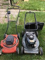 Two gas lawnmowers on grass: Craftsman mower dark green with black engine housing, Beaumark mower orange with black engine cover.