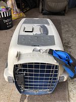 Top angled view of white and gray small pet carrier with Pet Taxi lettering and blue strap with baggie holder attached.